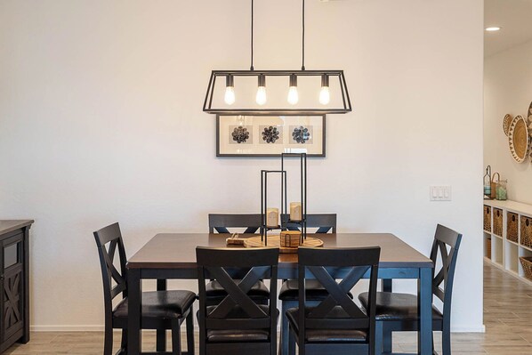 A dining area with a rectangular table, six black chairs, a pendant light fixture, and framed wall art above the table. - Queen Creek 30+ Night Stays | Private Heated Pool (Queen Creek)