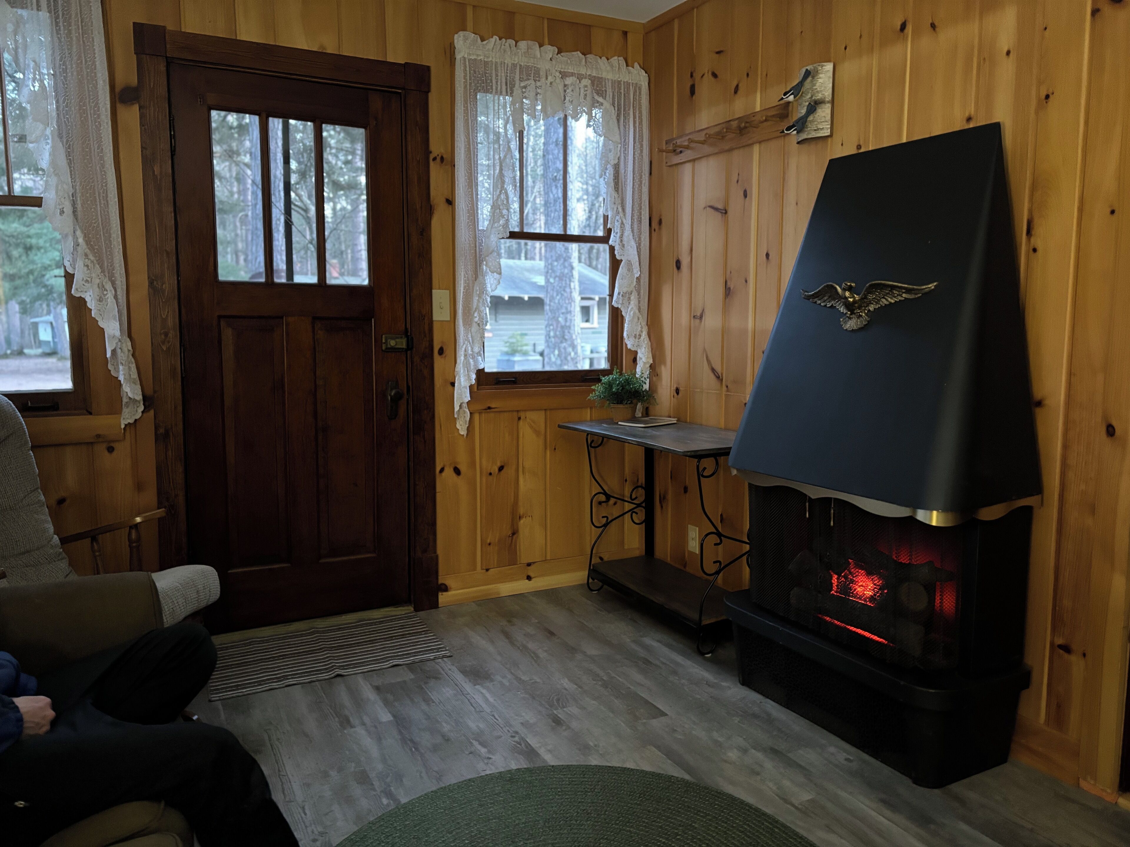 A cozy cabin interior with a wooden door, a fireplace, a small table, and a bench.