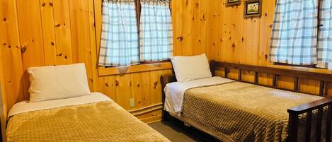 Habitación con dos camas, paredes de madera y ventanas con cortinas a cuadros.
