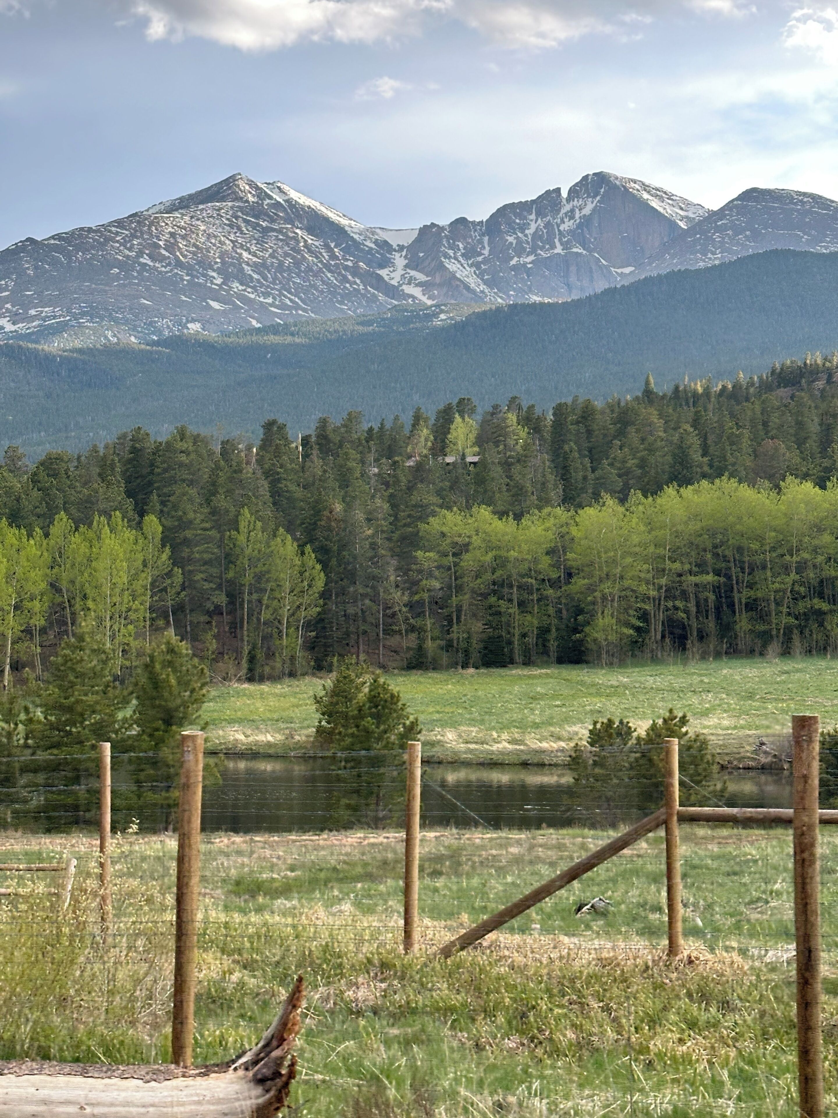 Un paisaje montañoso con un campo en primer plano y una valla de madera.