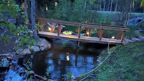 A wooden bridge over a stream with a picnic table in the foreground.