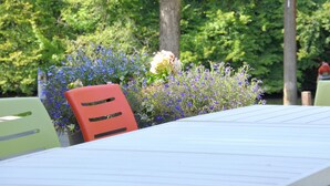 A table with a white tablecloth, surrounded by chairs, in a garden setting with various plants and flowers. - Holiday Home in Bouillon Near River Semois (Bouillon)