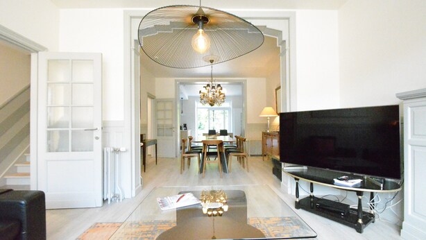 A spacious living room with a glass coffee table, a large flat-screen TV, and a chandelier. - Holiday Home in Bouillon Near River Semois (Bouillon)