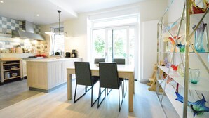 A modern kitchen with a central island, two black chairs, and a glass display of colorful vases. - Holiday Home in Bouillon Near River Semois (Bouillon)