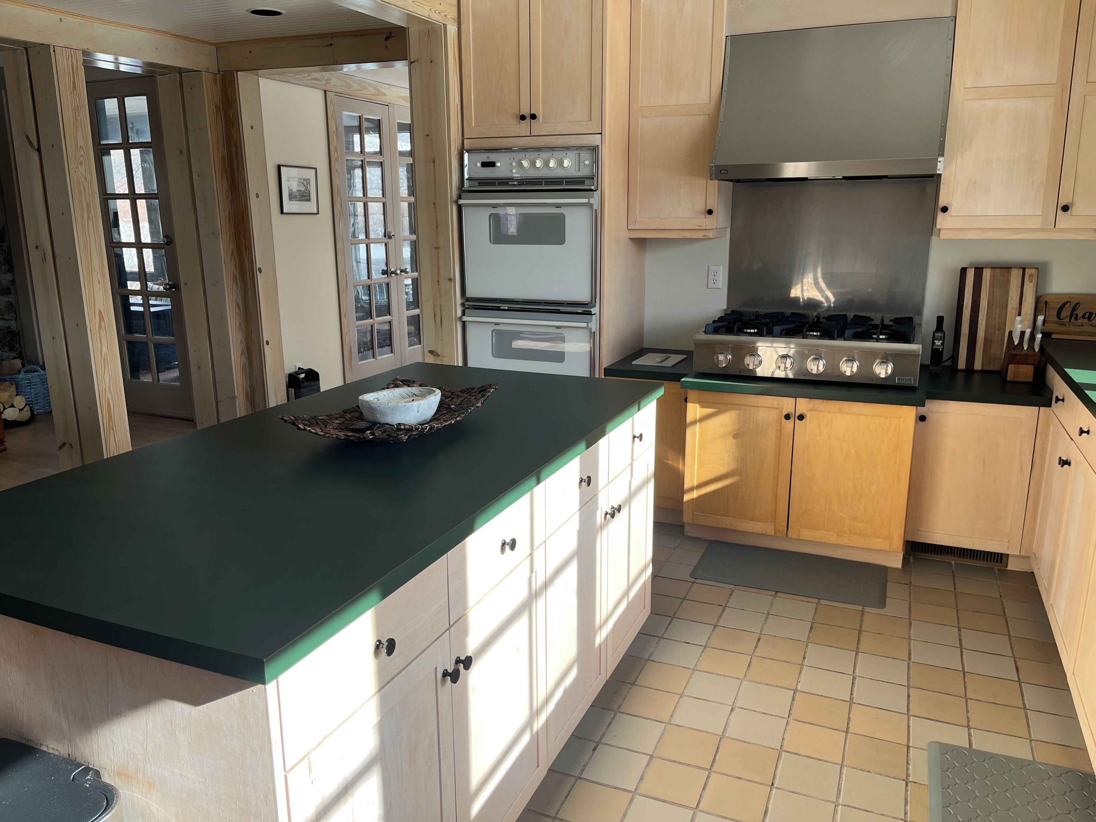 A kitchen with wooden cabinets, a green countertop, a stove, and a large window.