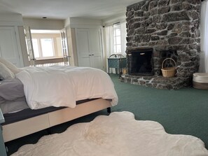 Un dormitorio con chimenea de piedra, una cama con ropa blanca y una alfombra verde.