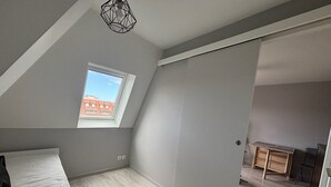 Una habitación con techo inclinado, tragaluz, cama, escritorio y armario.