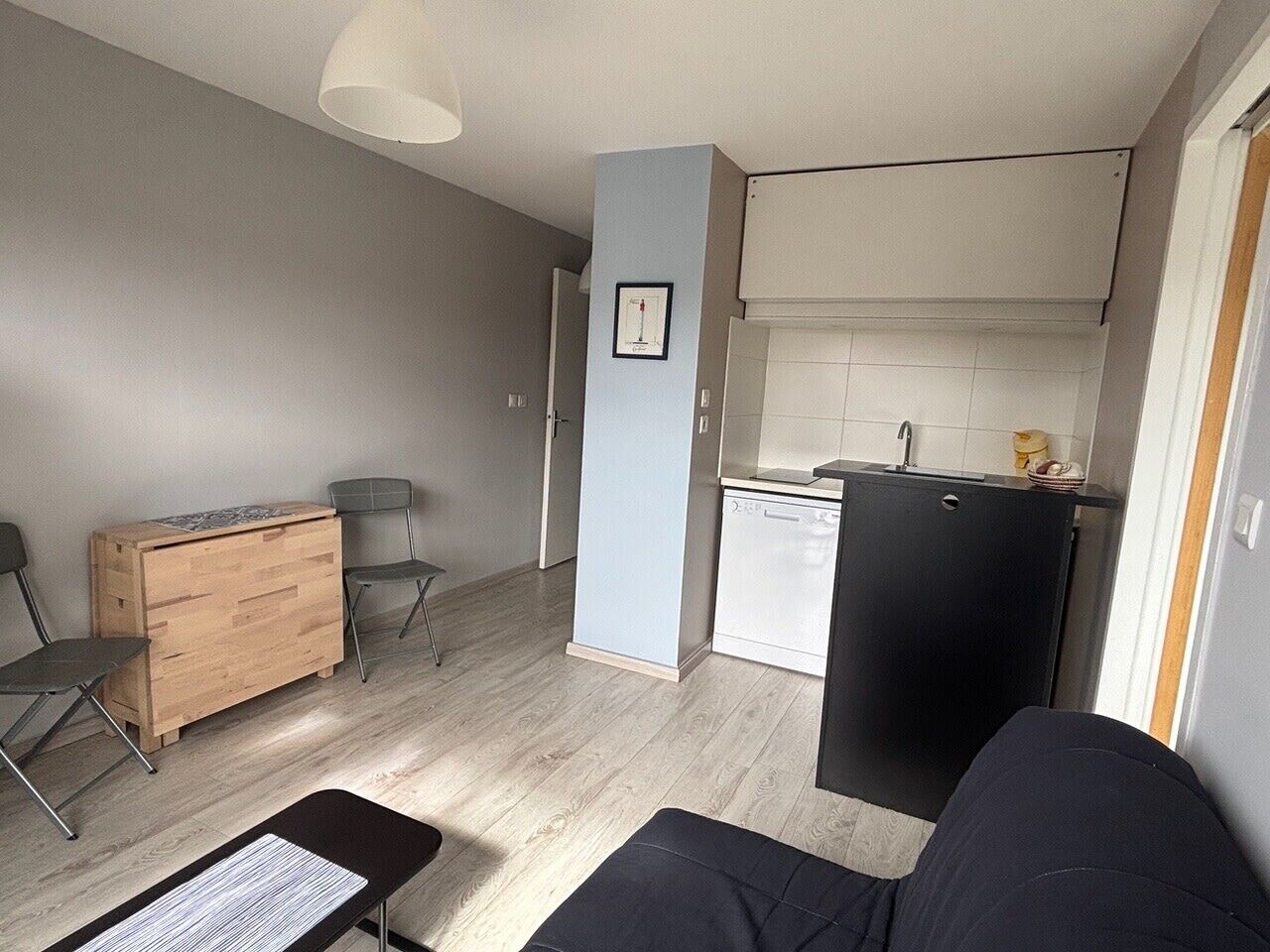 Un espacio habitable compacto con kitchenette, un aparador de madera, dos sillas y un sofá negro.