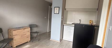 Un espacio habitable compacto con kitchenette, un aparador de madera, dos sillas y un sofá negro.