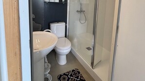Un baño pequeño con inodoro, lavamanos y ducha con mampara de vidrio.