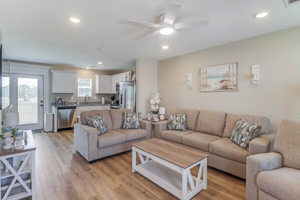 A modern living room with a beige sofa set, a wooden coffee table, and a kitchen in the background.