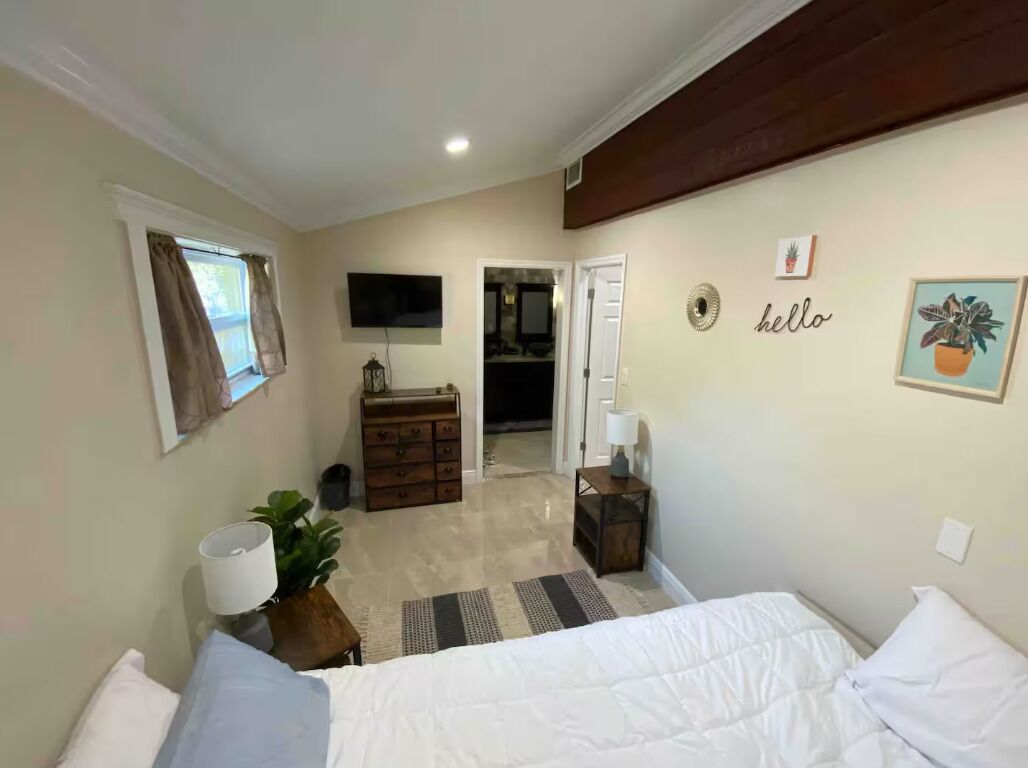A bedroom with a bed, a dresser, a mirror, a television, and a door leading to another room.