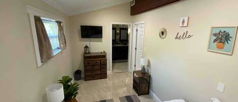 A bedroom with a bed, a dresser, a mirror, a television, and a door leading to another room.
