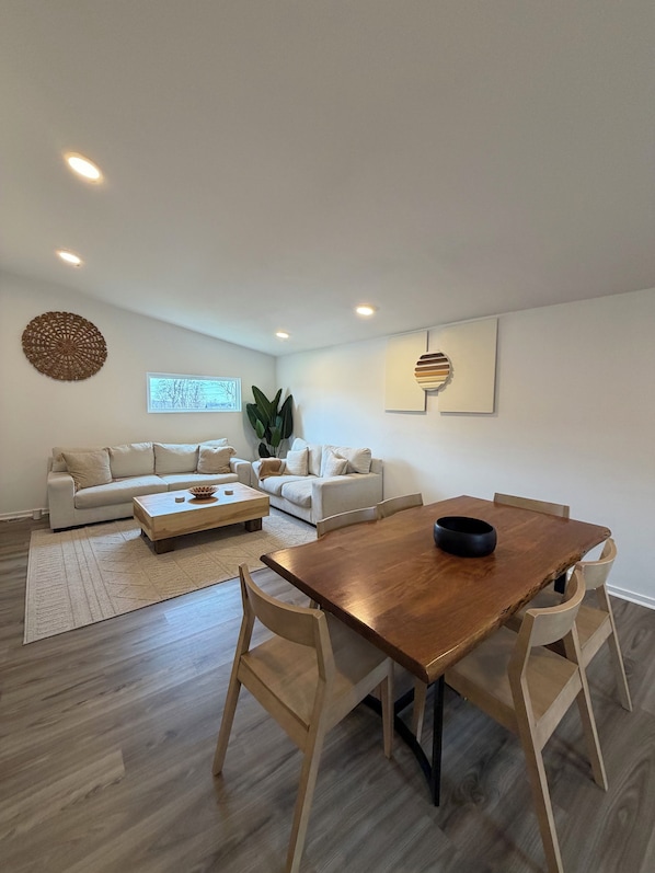 Een moderne woonkamer met een houten eettafel, twee banken, een salontafel en een grote plant.