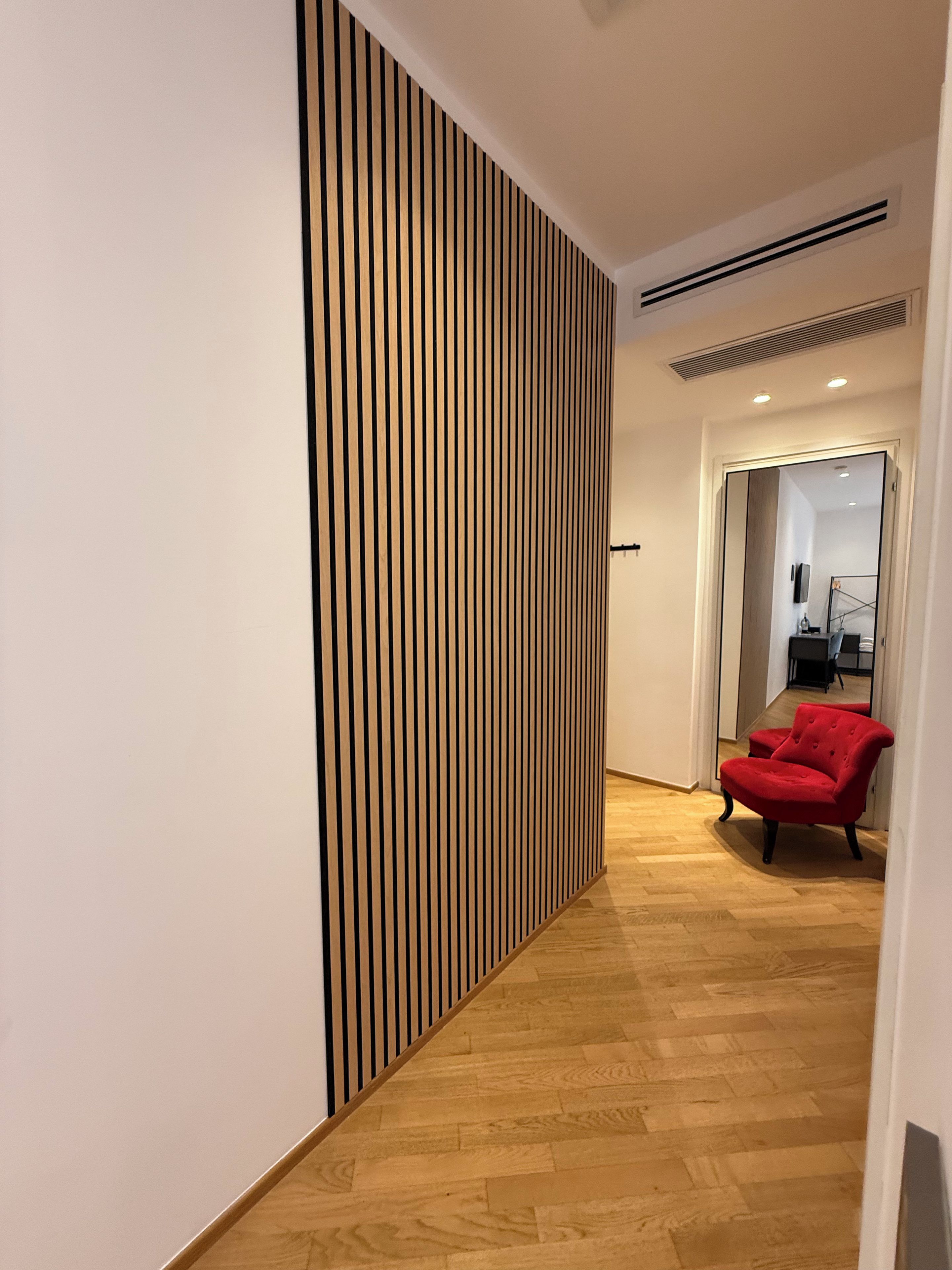 A hallway with a wooden slat wall, a red chair, and a wooden floor.