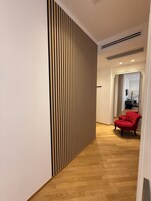 A hallway with a wooden slat wall, a red chair, and a wooden floor.