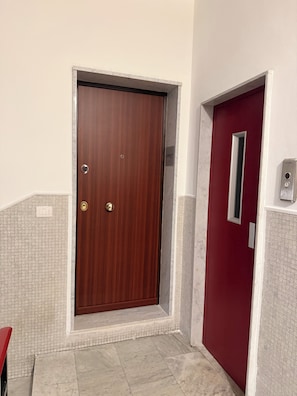 A wooden door with a keypad lock, a red door with a window, and a tiled floor. - Cosy (Bari)