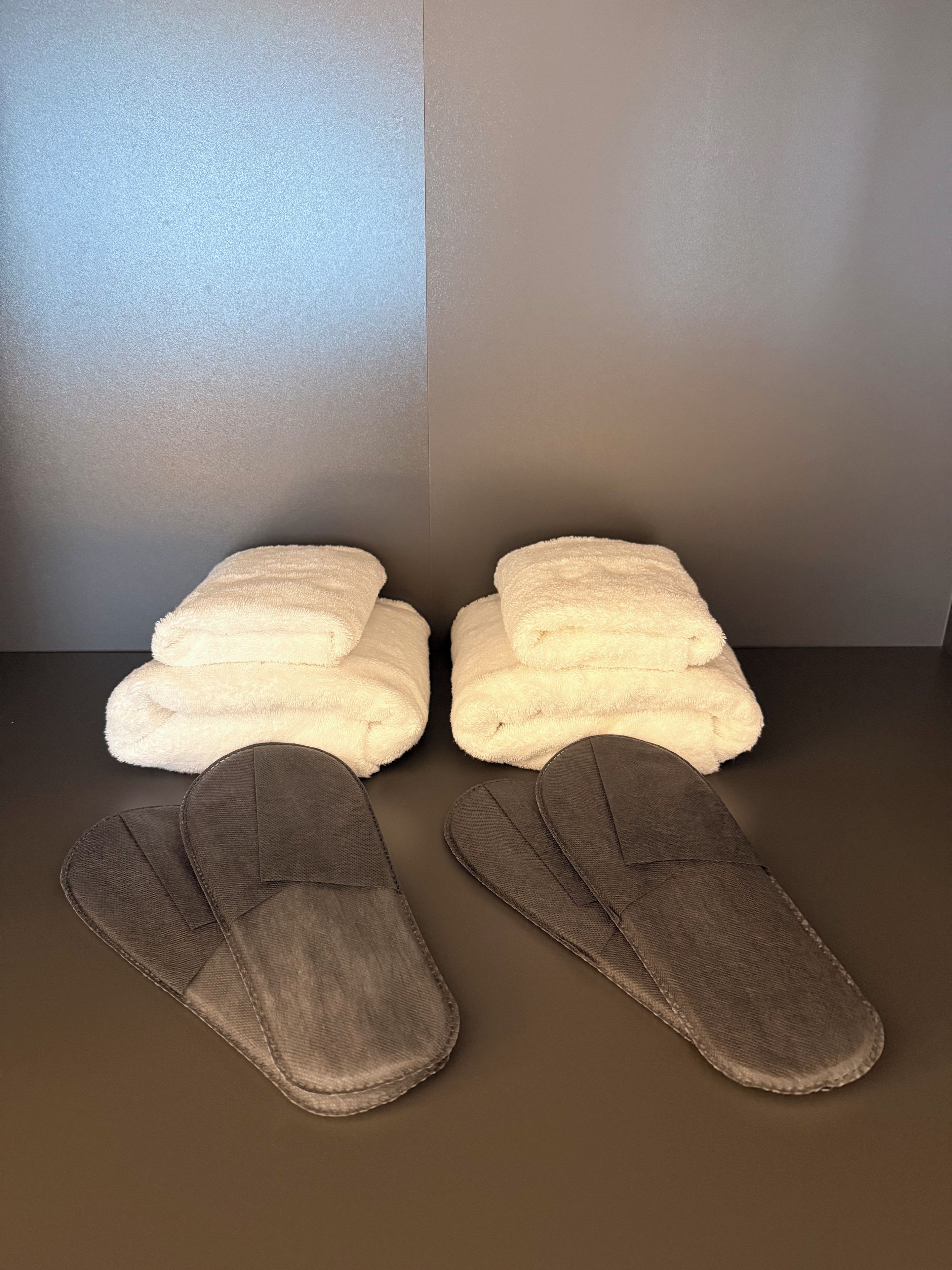 A pair of white towels and two brown slippers on a dark surface.