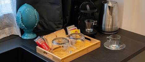 A kitchen counter with a coffee maker, a kettle, a tray with bread, and a glass cup.