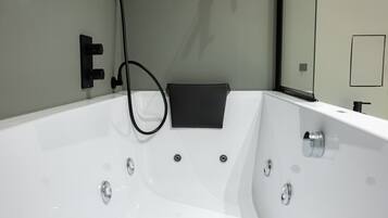 Un baño moderno con una bañera grande, una toalla negra y un espejo.
