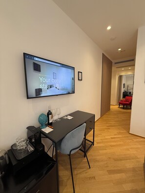 Habitació d'hotel moderna amb televisió de pantalla plana penjada a la paret que mostra un missatge, una taula de treball amb una cadira, una petita cuina i una cadira vermella al fons.