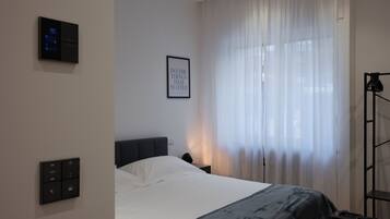 Quarto de hotel moderno com cama, painel de controle, citação inspiradora emoldurada e uma grande janela com cortinas translúcidas.