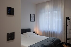 A modern hotel room with a bed, a control panel, a framed inspirational quote, and a large window with sheer curtains. - Cosy (Bari)