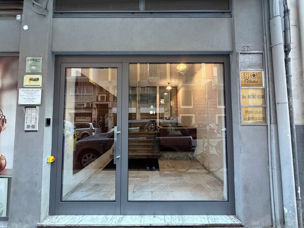Une entrée d’immeuble avec une porte en verre, une enseigne indiquant « ENJOY Pilates » et une autre indiquant « STUDIO LEGALE ».