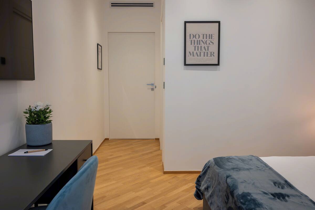Una habitación de hotel con una cama, un escritorio con una silla, una planta en maceta y un cartel motivacional en la pared.