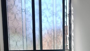 A room with a crib, a small table with a cactus, and a window with decorative curtains. - The Rose of Pompeii (Scafati)