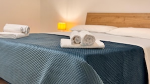 A neatly made bed with a blue textured bedspread, two rolled white towels, and a lit bedside lamp. - The Rose of Pompeii (Scafati)