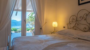 A bedroom with a bed, curtains, a lamp, and a view of the outdoors.