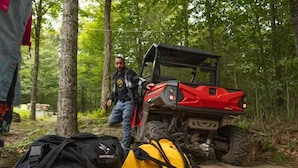 A red off-road vehicle parked in a forested area with a black and yellow backpack on the ground. - Riverfront Bell Tent Glamping -15 minutes to Bethel Woods Concerts (Harris)