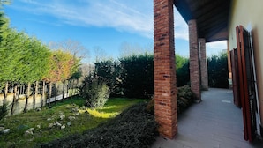 A covered outdoor area with brick pillars, a pathway, and a garden with trees and shrubs. - CR BnB Rozzano (Rozzano)