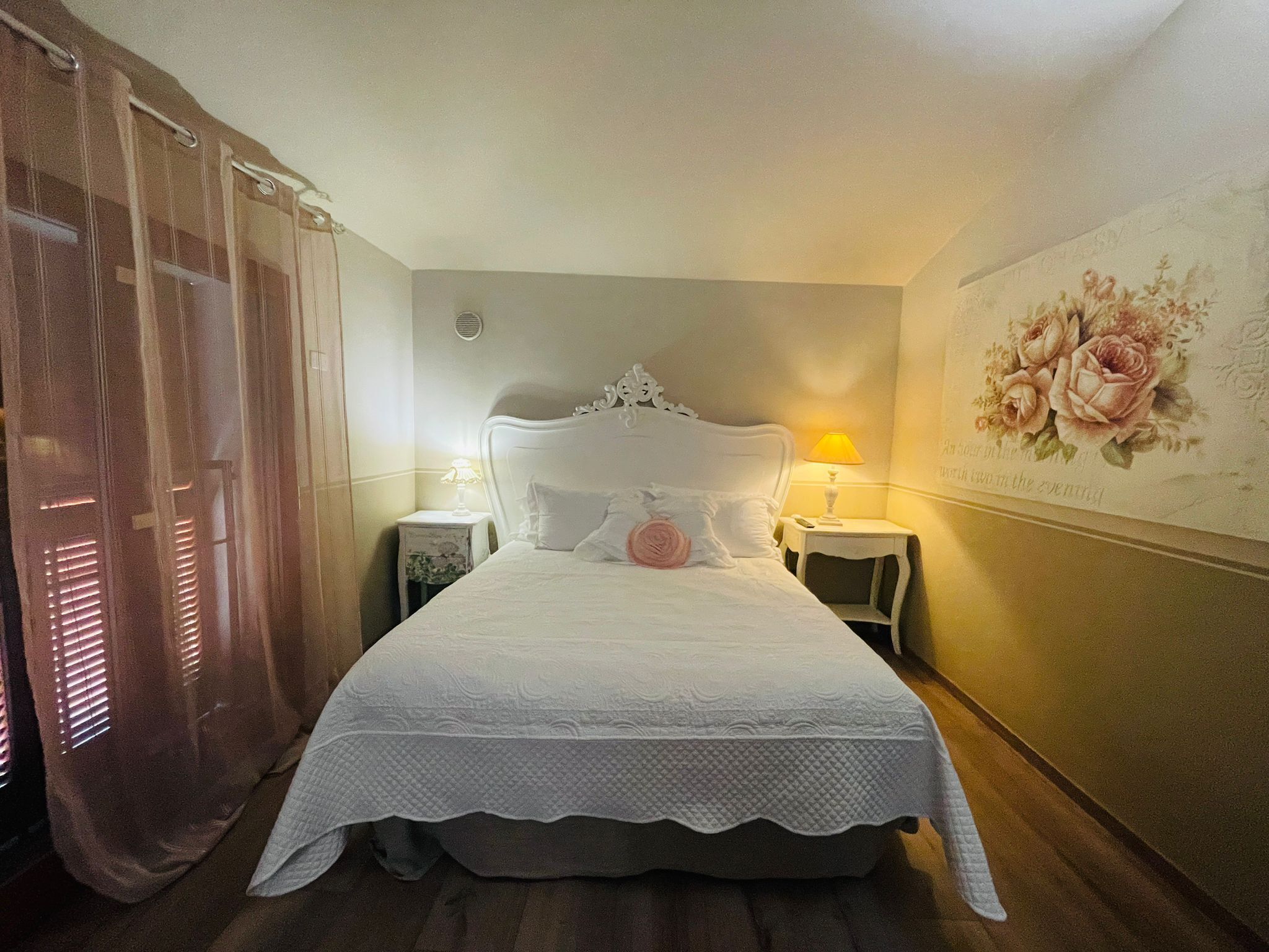 Un letto rifatto con una testiera bianca, due comodini con lampade e carta da parati a motivi floreali sulla parete.