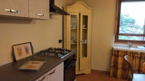 A kitchen with a gas stove, wooden cabinets, a glass-fronted cabinet, and a window with curtains. - Il Corridore - Piccolo Borgo Tralacoasta (Berceto)