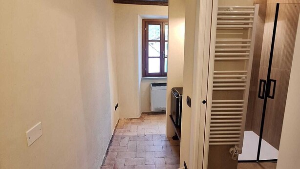 A narrow hallway with a tiled floor, a window at the end, and a radiator. - Il Corridore - Piccolo Borgo Tralacoasta (Berceto)