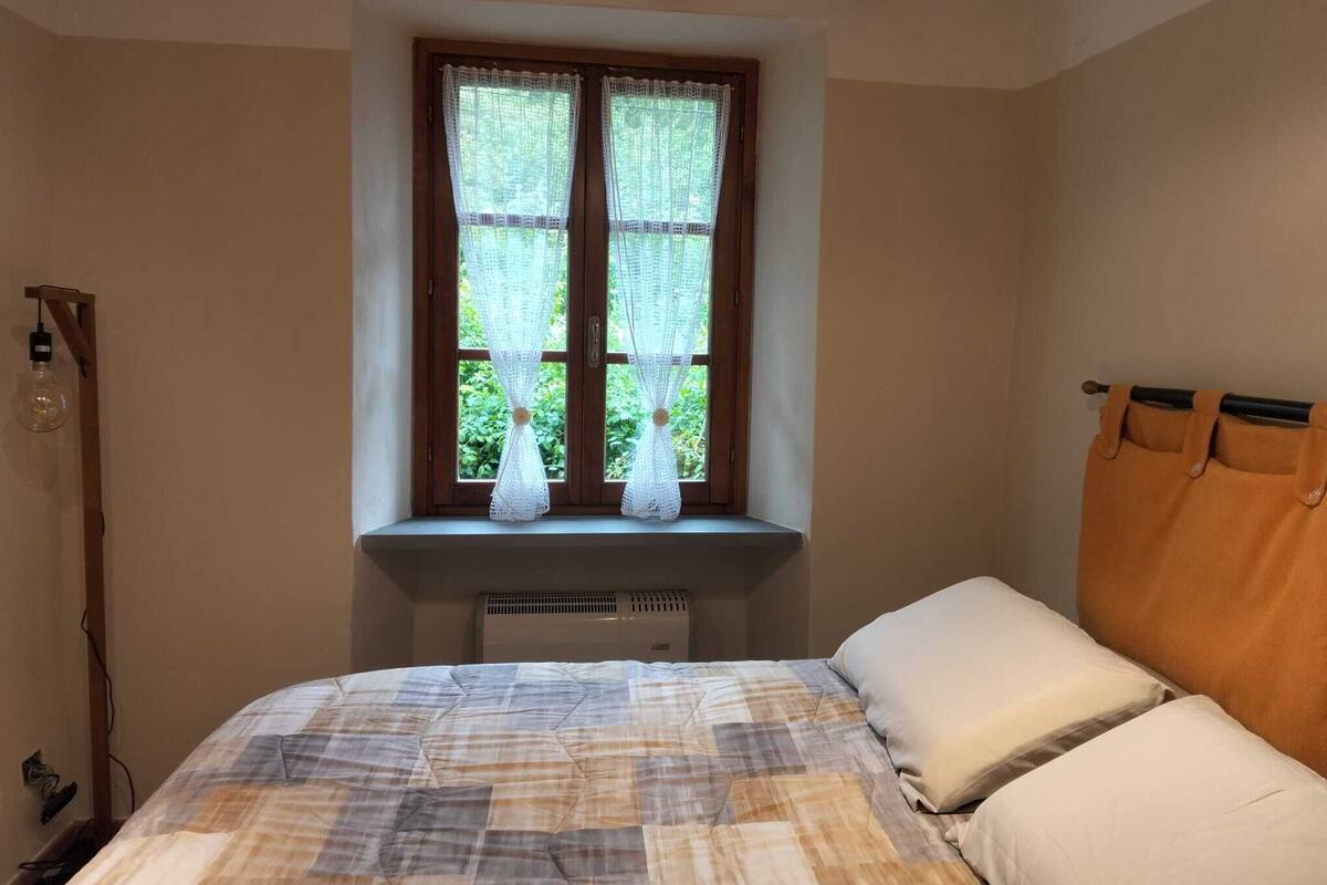 A bedroom with a bed, a window with lace curtains, a wooden headboard, and a radiator.