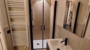 A bathroom with a tiled floor, a sink with a mirror, a towel rack, and a shower area. - Il Corridore - Piccolo Borgo Tralacoasta (Berceto)