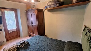 A bedroom with a bed, wooden wardrobe, and a shelf with a wrapped item. - Il Corridore - Piccolo Borgo Tralacoasta (Berceto)
