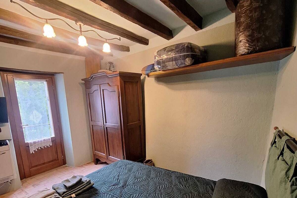 A bedroom with a bed, wooden wardrobe, and a shelf with a wrapped item.
