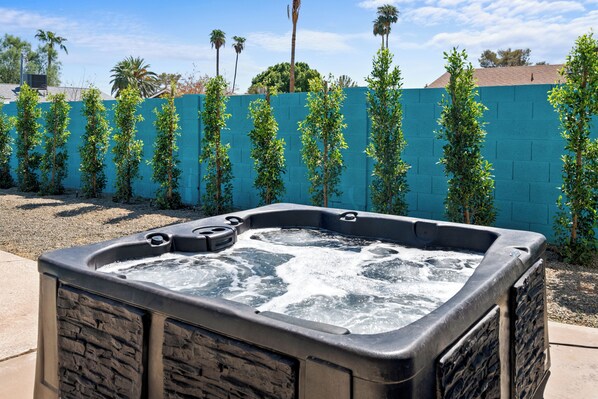 A hot tub with a stone facade, surrounded by a blue wall and greenery.