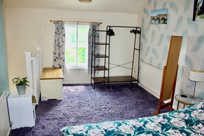 A bedroom with a bunk bed, a window with curtains, a radiator, a bedside table with a lamp, and a floral bedspread.