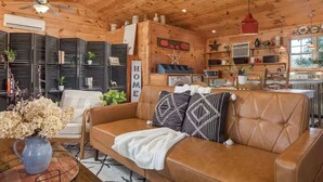A cozy living room with a brown leather sofa, a white chair, and a blue vase with flowers. - Liberty Lodge Countryside Stay! Hot Tub, Sunsets (Valley Head)