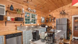 A compact kitchen with wooden walls, a dishwasher, a coffee maker, and a refrigerator. - Liberty Lodge Countryside Stay! Hot Tub, Sunsets (Valley Head)
