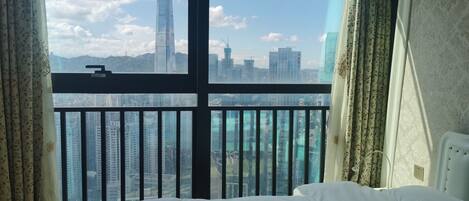 A hotel room with a large window offering a cityscape view, a bed, and curtains.