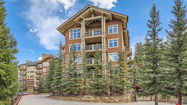 A multi-story residential building with balconies, surrounded by evergreen trees and a stone circular feature. - Luxurious Ski-In/Ski-Out Condominium in the Heart of Mountain Paradise (Keystone)