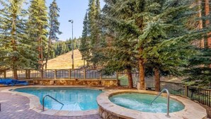 A pool area with two hot tubs, surrounded by trees and a stone wall. - Luxurious Ski-In/Ski-Out Condominium in the Heart of Mountain Paradise (Keystone)