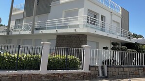 Une maison moderne à deux étages, dotée d’un balcon, de fondations en pierre et d’une clôture blanche.