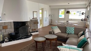 Un salon moderne avec une cheminée en pierre, un canapé en cuir et un coin repas comprenant une table et des chaises.